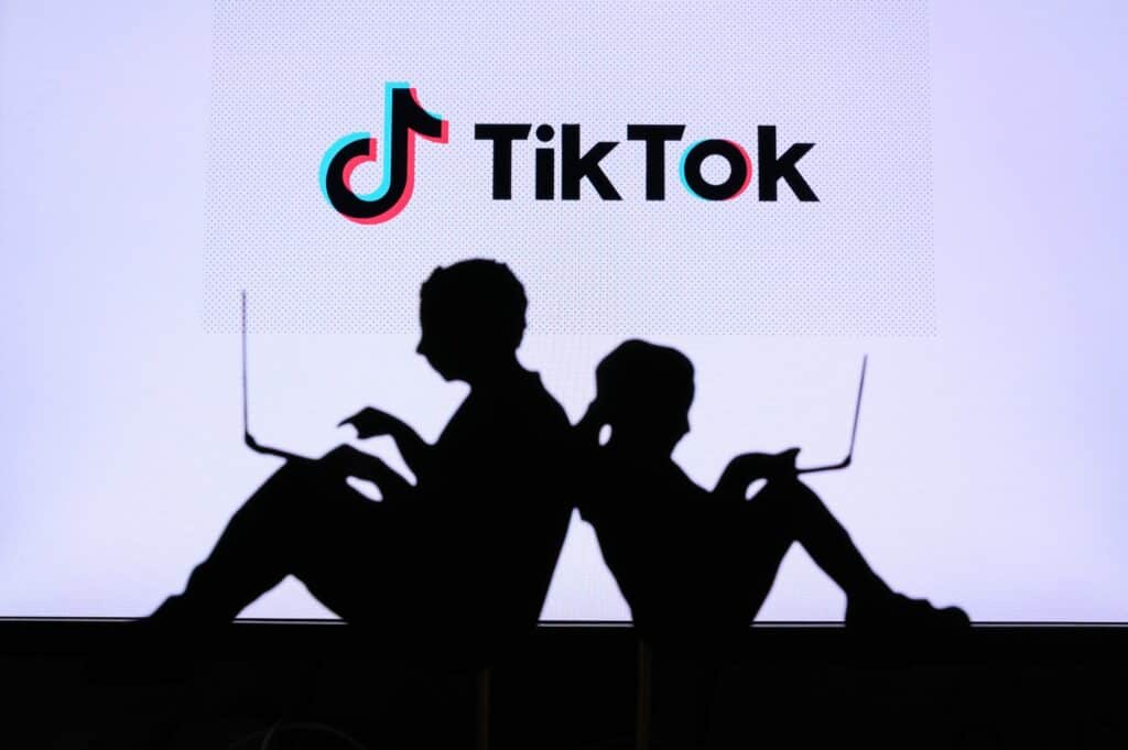Deux silhouettes noires d'enfants assis, l'une d'un garçon et l'autre d'une petite fille entrain d'utiliser chacun un ordinateur portable. Sur le dessus, le logo de TikTok