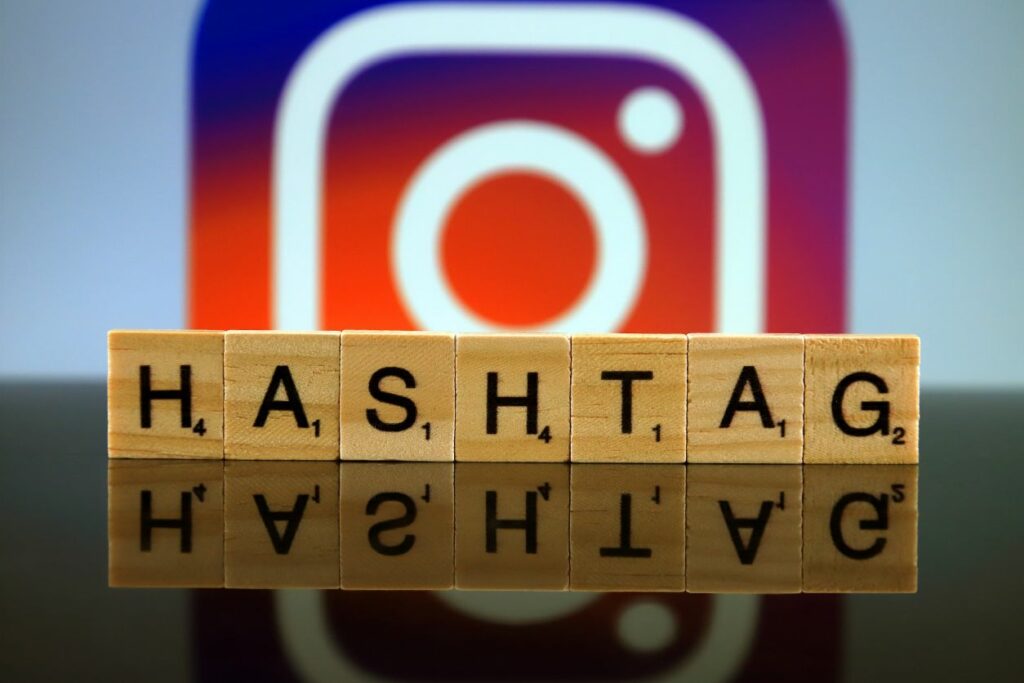 "hashtag" inscrit en lettres majuscules sur des cubes alignés à l'horizontale, logo Instagram en arrière plan au dessus des cubes
