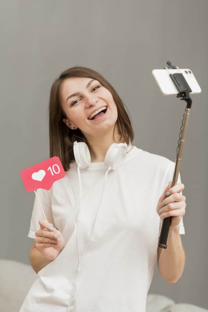 Une jeune femme souriante tenant un smartphone avec une perche pour faire une vidéo.